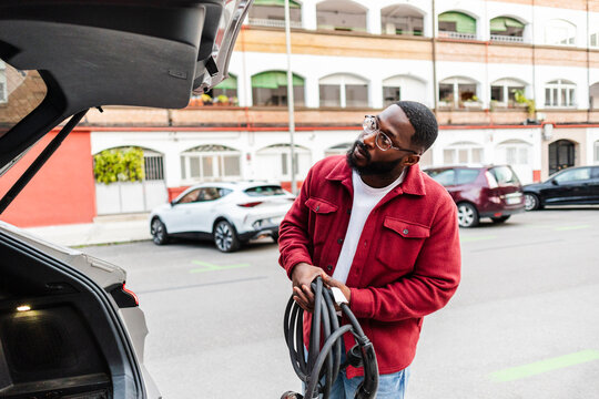 Man charging electric car on urban street in daytime