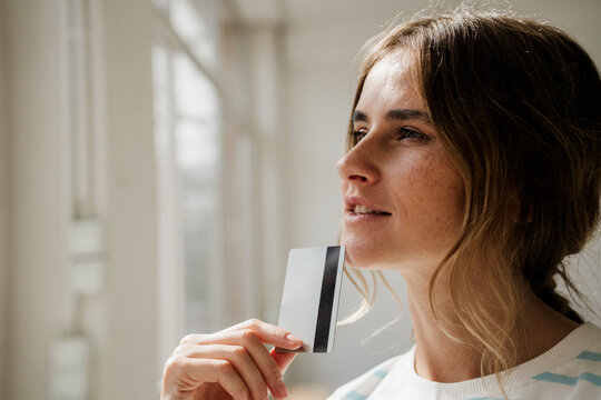 Person thinking with credit card by window in creative studio