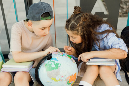 Children studying globe and books outdoors in summer sunlight
