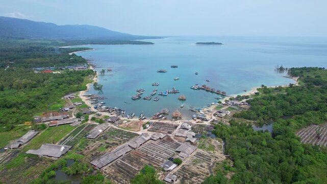 Aerial drone footage of Sumur port bay, in Pandeglang regency, Java island, Indonesia, with dry fish farms and people working, wooden fishing huts in construction, with blue reef waters, white sand