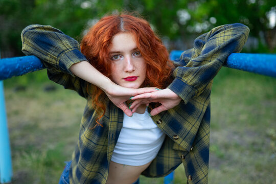 Red haired woman posing on parallel bars at old playground outdoors