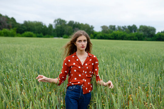 Woman in red polka dot blouse standing in wheat field outdoors
