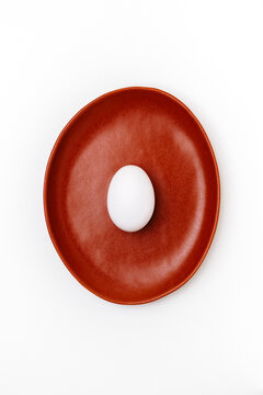 White egg on brown plate in minimal studio still life