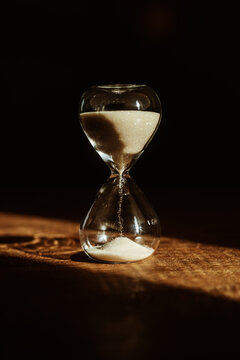 Hourglass with sand in sunlight on wooden surface emphasizing time