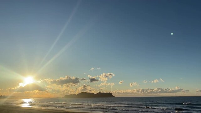 雲から出てきた朝日と朝焼けの残る青空とシルエットの江ノ島