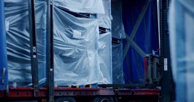 Close up of forklift mast and forks unloading a pallet wrapped in plastic from a truck trailer