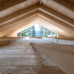 Vue en perspective de l'intérieur de combles en bois clair avec fenêtre sur forêt