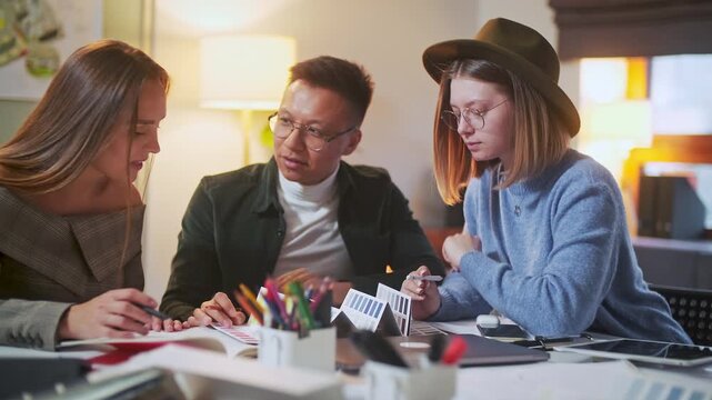 Professional creative team discussing project ideas together in a warm modern office. Women and man, coworkers, colleagues or specialists sharing feedback, reviewing materials, planning tasks or