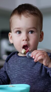 Lovely baby boy blows on his food and then puts it in his mouth. Toddler eating from fork. Blurred backdrop. Vertical video