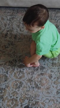 Lovely baby boy pushing his toy train by the carpet. Toddler plays at home. Top angle perspective. Vertical video