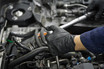 Fototapeta premium Mechanic in black gloves repairs car engine with wrench