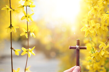 Easter concept featuring a cross symbolizing the suffering, death, and resurrection of Jesus Christ, and a background of beautiful forsythia flowers. 