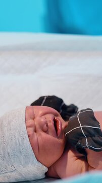 Newborn wearing mittens, socks and cap lies on the table crying. Nurse outs on a diaper on a baby. Vertical video