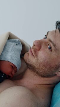 Caucasian father holding his newborn baby on the bare chest. Little child cries bitterly. Infant born through C-section. Vertical video