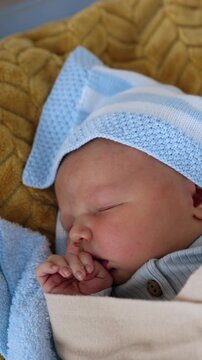 Cute sleeping newborn baby boy lies in a crib. Child in blue blanket holding tiny hand near the mouth. Top view. Vertical video