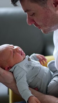 Little newborn boy is crying in dad's hands. Father tries to sooth his child waving him. Vertical video