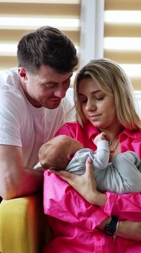 Young Caucasian parents with their child in maternity hospital. Mother rocks her baby boy and father sits beside. Vertical video