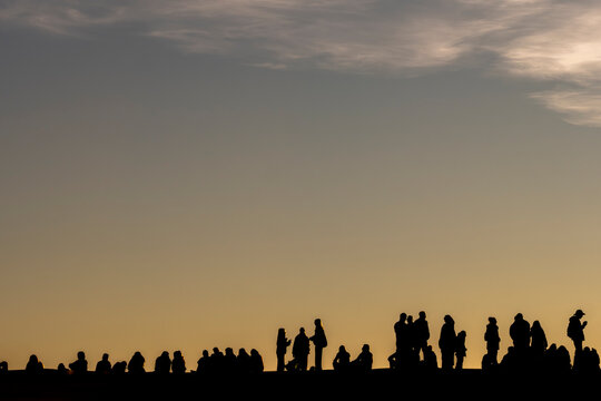 Dusk gathering outdoors with people forming a crowd silhouette under sunset sky near the horizon creating calm landscape mood for community