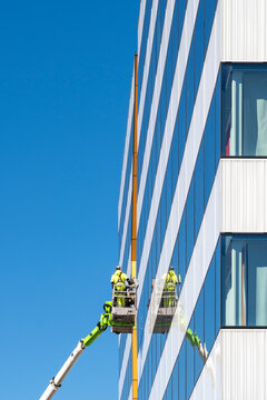 Urban building glass facade window cleaning by worker at height with safety maintenance focus showing professional city service work