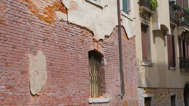 Navigating venetian canals: observing deteriorating brick walls. Historic venetian canal featuring weathered brick walls, revealing architectural decay through intricate details of crumbling textures