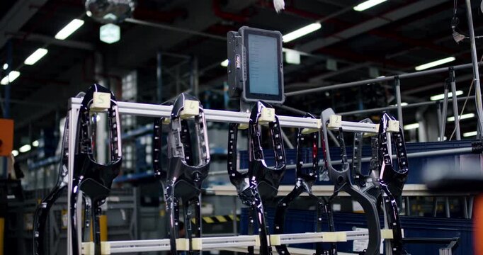 Row of black plastic car interior parts hanging on an automated assembly line with a digital monitor in a factory