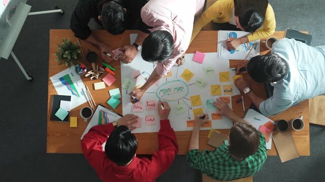 Group of business people writing sticky note and making mind map to brainstorming marketing idea at meeting. Top aerial view of investors sharing plan or strategy and stick note at paper. Convocation.