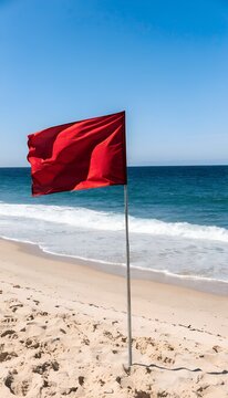 red flag signals warning on sandy beach alongside clear blue ocean and cloudless sky