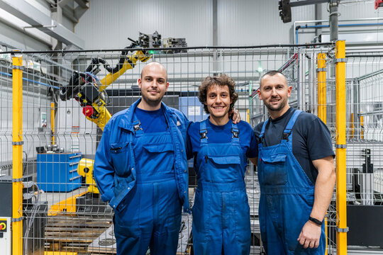 Smiling engineering colleagues in front of machinery with robotic arm at modern factory