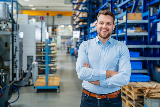 Smiling employee standing arms crossed in modern production hall