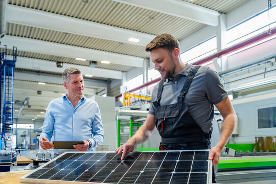 Engineer and coworker inspecting solar panel in production hall