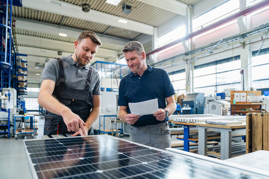 Employees analyzing solar panel in production hall during meeting