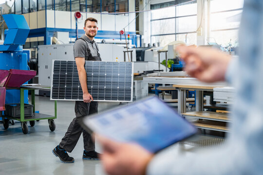 Employee carrying solar panel in production hall during business meeting