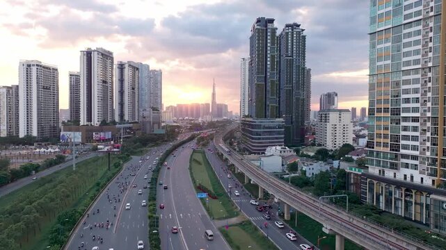 Aerial drone view of Metro train passing highway at sunset in Ho Chi Minh City with Landmark 81 skyline