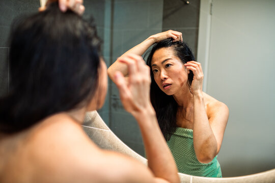 Woman examining her hairline in bathroom mirror
