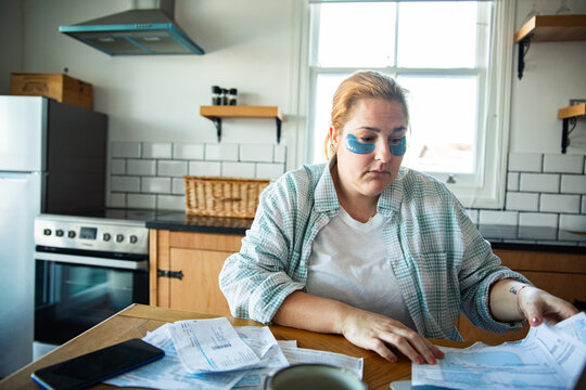 Woman with under-eye patches reviewing bills at kitchen table
