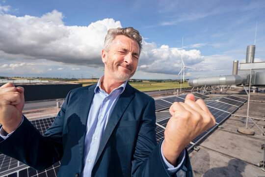 Carefree businessman with eyes closed celebrating on terrace with solar panels