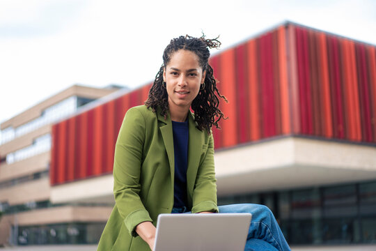 Confident businesswoman using laptop sitting at office park