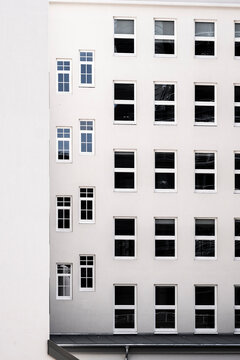 Minimalist urban facade of a modern white building with repeating windows forming clean geometric architecture pattern in daylight
