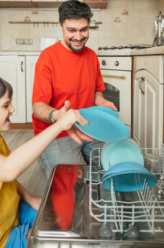 Father and child loading dishwasher together in home kitchen