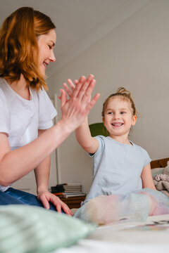Mother and daughter smiling and high fiving together at home