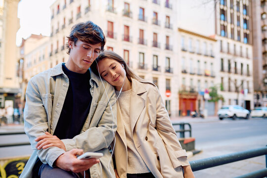 Young couple enjoying time together in an urban setting, sharing music from a smartphone and wearing wired earphones
