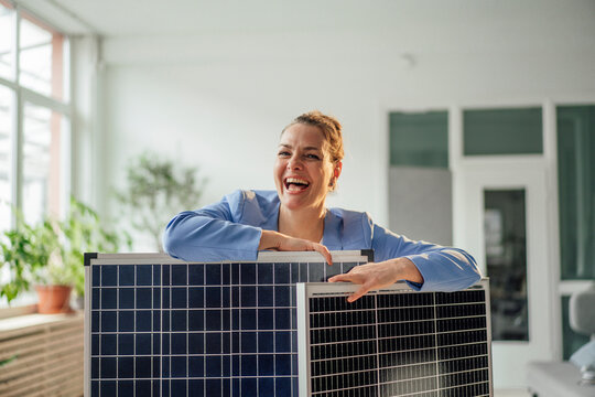 Happy mature businesswoman leaning on solar panels in office