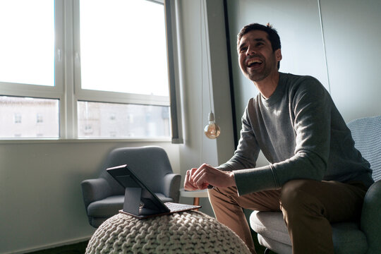 Happy businessman sitting with tablet PC in office
