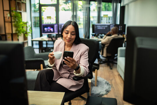 Smiling businesswoman checking smartphone during coffee break in modern office