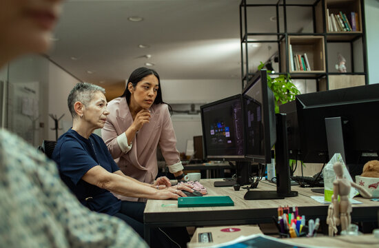 Two women coworkers collaborating at computer in modern office