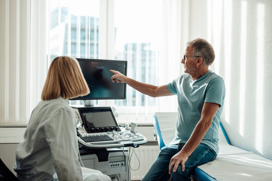 Patient pointing at ultrasound monitor consulting doctor indoors