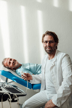 Smiling doctor with ultrasound machine and patient in hospital