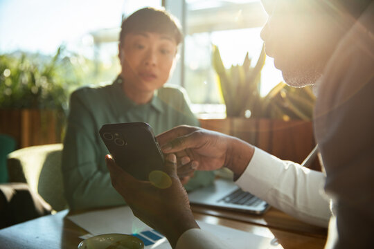 Two coworkers discussing a project on a smartphone at a cafe