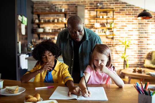 Tutor helping children with homework at kitchen table