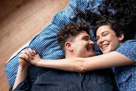 Romantic man holding hand of girlfriend lying on bed at home